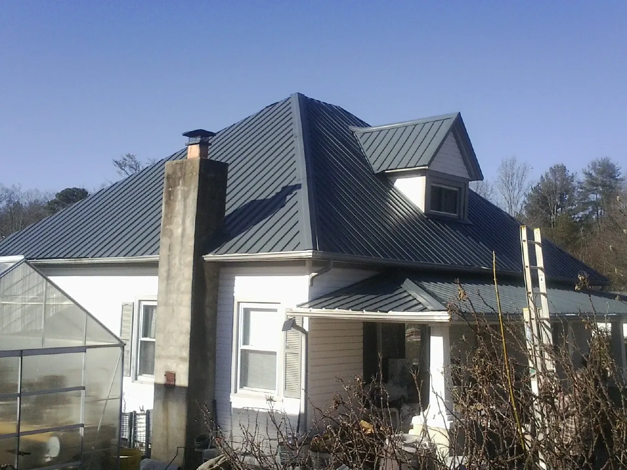 Dark blue standing seam metal roof on a white farmhouse with dormer — Slate & Tile Roof Repair by Roofing Brothers in Cary