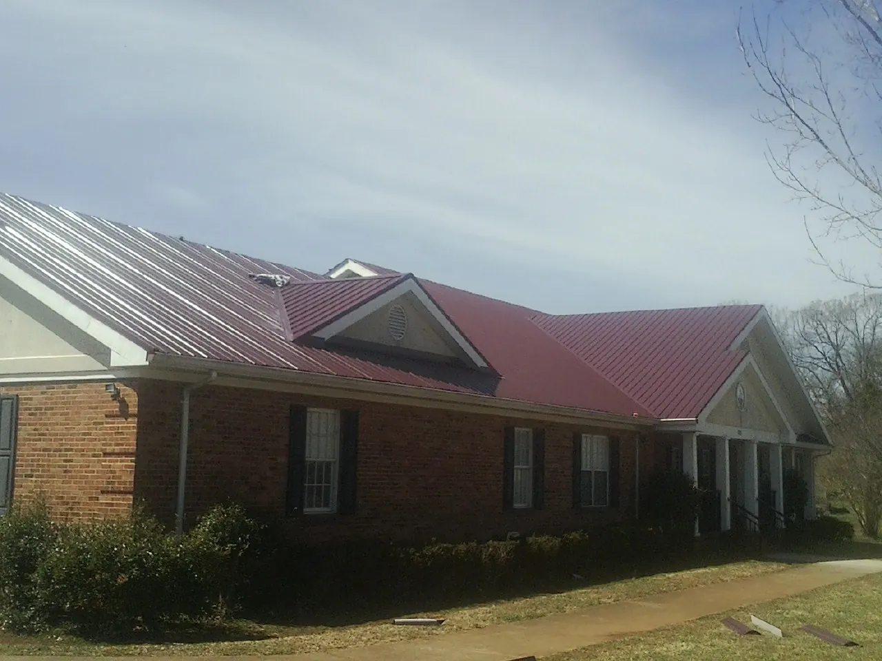 Red metal roof with gabled entries on a long brick building, from a Hail Damage Roof Repair job in Cary