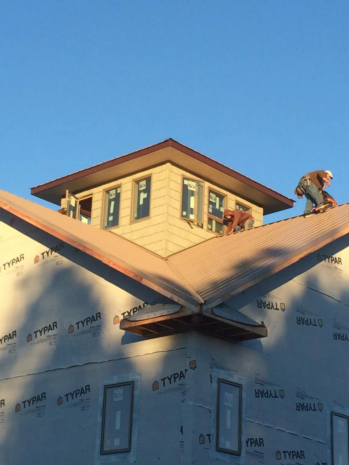 Roofers working around a rooftop cupola on a new metal roof at sunset — Roof Waterproofing in Cary by Roofing Brothers